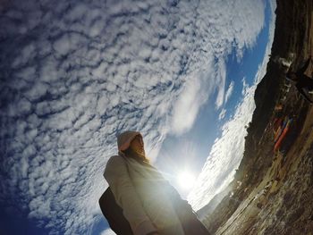 Tilt image of hiker standing on field against cloudy sky