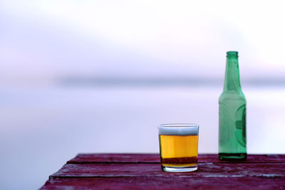 Glass of bottle on table by sea