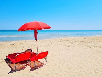 Deck chairs on beach against clear blue sky