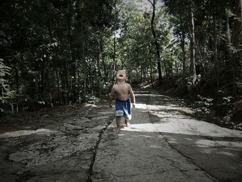 Shirtless boy walking on footpath amidst trees