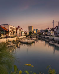 River by buildings against sky during sunset