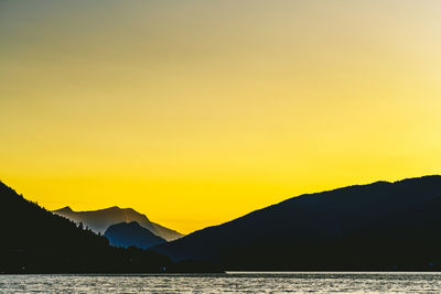 Silhouette mountains by sea against romantic sky at sunset