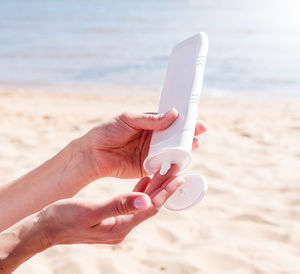 Young caucasian woman applying sun cream sunbathing on beach. mockup of sunscreen bottle