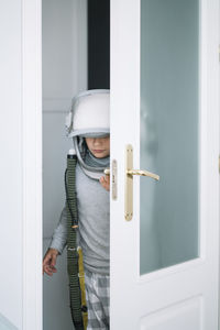 Busybody kid with helmet looking through the crack in the door with funny annoyed expression