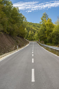 Empty road amidst trees against sky