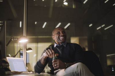 Happy businessman with juice bottle sitting in office at night