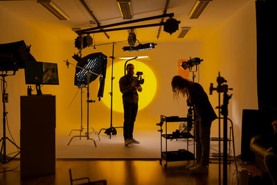 Professional videographer holding photo equipment and recording video of young woman dancer