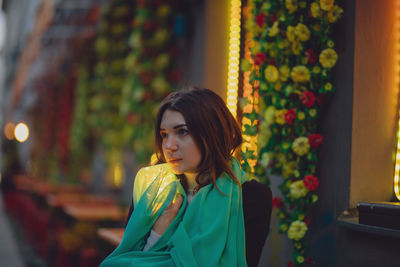 Thoughtful woman holding scarf and glowing jar in city at dusk