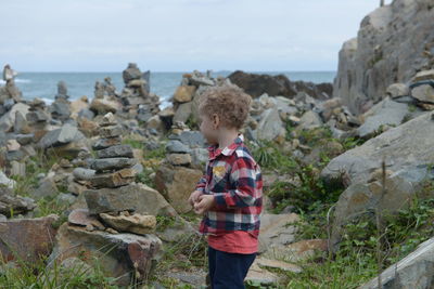 Side view of boy standing on rock at beach against sky