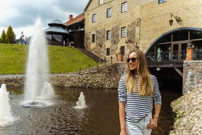 Smiling long-haired woman in a striped jumper near the fountain in summer