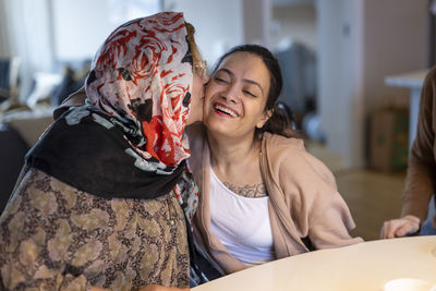 Mature woman kissing daughter with paraplegia sitting at home