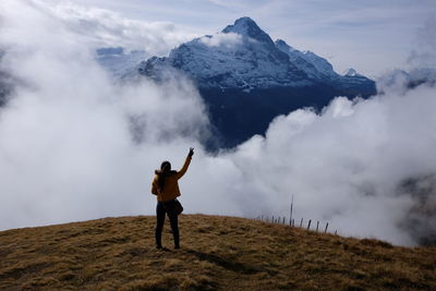 Rear view of woman standing on mountain peak against sky