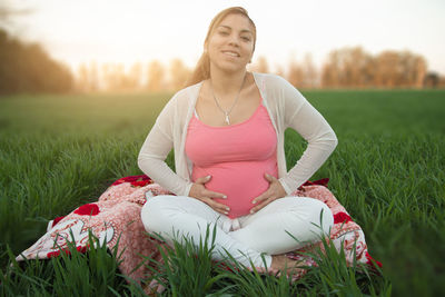 Young pregnant woman sitting on field