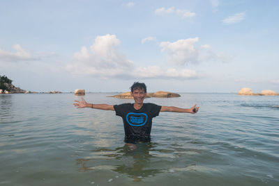 Portrait of mid adult man with arms outstretched standing in sea against sky