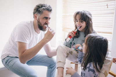 Father and daughters brushing teeth together in bathroom at home