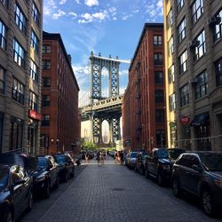 City street by manhattan bridge against sky