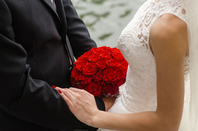 Midsection of couple holding hands while standing with bouquet