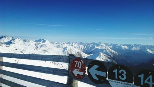 Signs on wooden railing at snowcapped mountain against blue sky