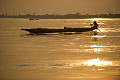 Silhouette man in boat on sea against sky during sunset