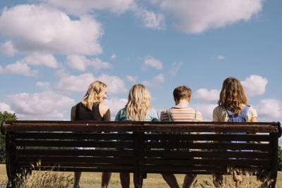 Friends sitting together on park bench under cloudy sky