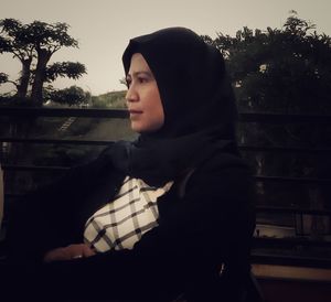 Portrait of young woman looking away while standing against trees