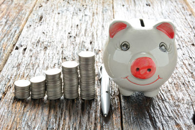 Close-up high angle view of coins by piggybank on table