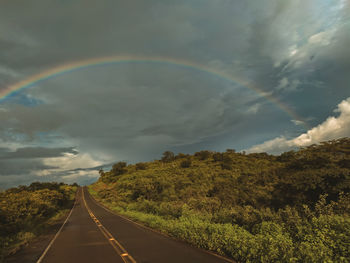 Rainbow over road against sky