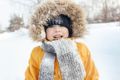 Smiling child in a fur hood in a knitted scarf and an orange winter jacket. 
