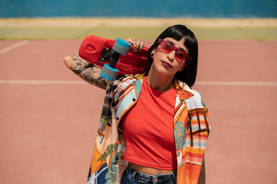 Caucasian girl with tattoos and short black hair on a sports ground with a skateboard in her hands