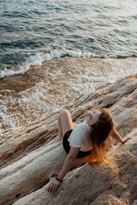 Rear view of woman sitting on rock at beach