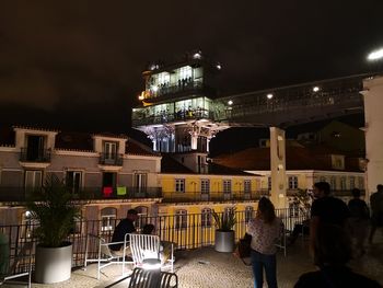 People on illuminated street amidst buildings in city at night