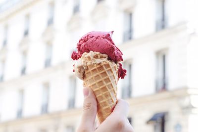 Close-up of hand holding ice cream cone against built structure