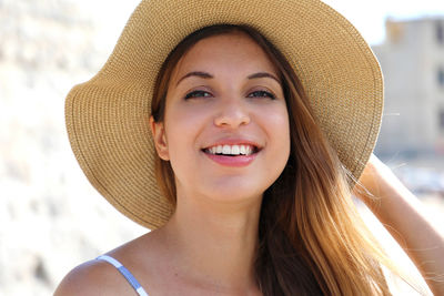 Close-up portrait of smiling young woman wearing hat standing in city