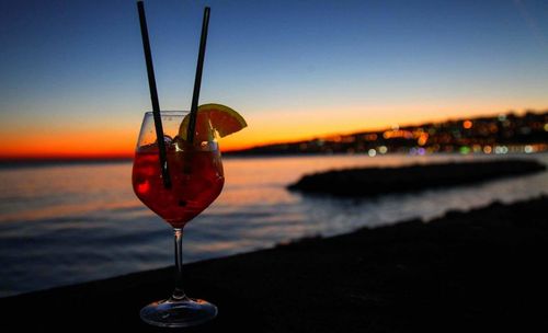 Close-up of wineglass on beach against sky during sunset