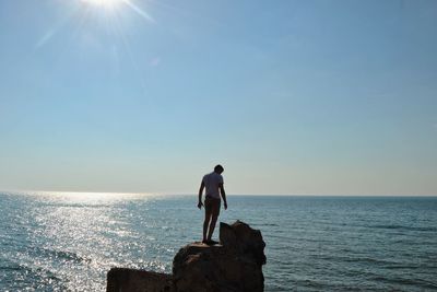 Man standing on rock by sea against sky