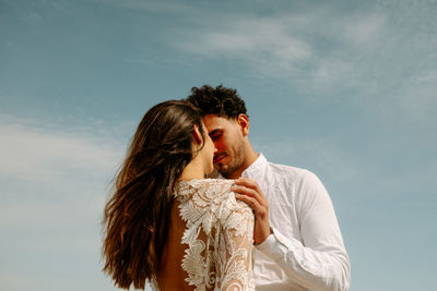 Young couple kissing against sky