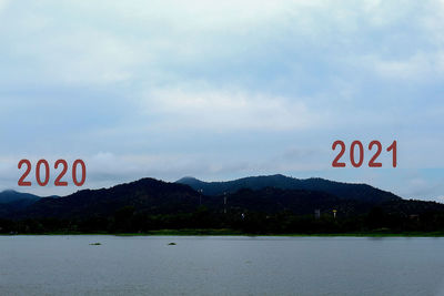 Information sign by lake against sky