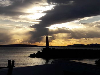 Silhouette lighthouse by sea against sky during sunset