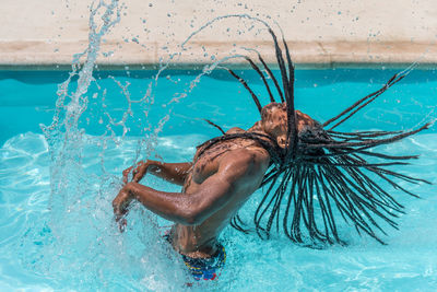 Black man with dreadlocks inside a pool raising his wet hair making a trail of water