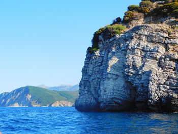 Rock formations in sea against clear blue sky