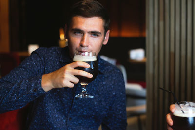 Handsome young man in a bar. the boy enjoys a dark beer. there is a pleasant atmosphere for fun. 