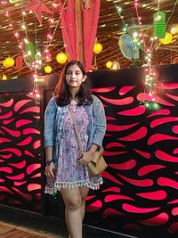Portrait of smiling young woman standing against illuminated wall