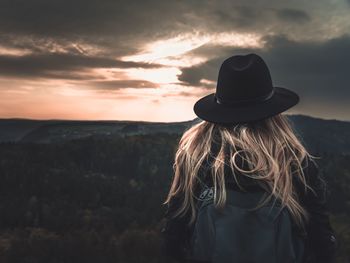 Rear view of woman looking at mountain against cloudy sky during sunset