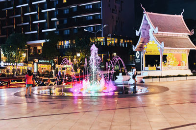 Illuminated fountain by building in city at night