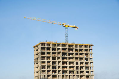 Low angle view of crane by building against clear blue sky