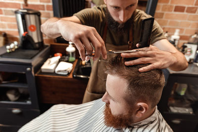 Barber cutting hair of man in salon