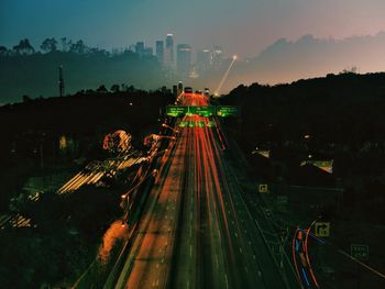 High angle view of highway light trails at sunset against cityscape