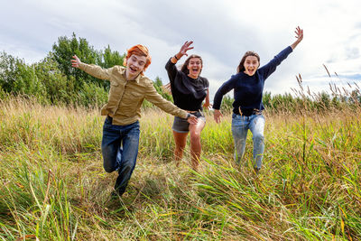 Group of three friends boy and two girls running and having fun together outdoors