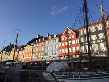 Sailboats moored on canal by buildings against blue sky