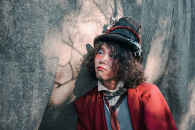 Portrait of young man cosplaying mad hatter looking away against statue